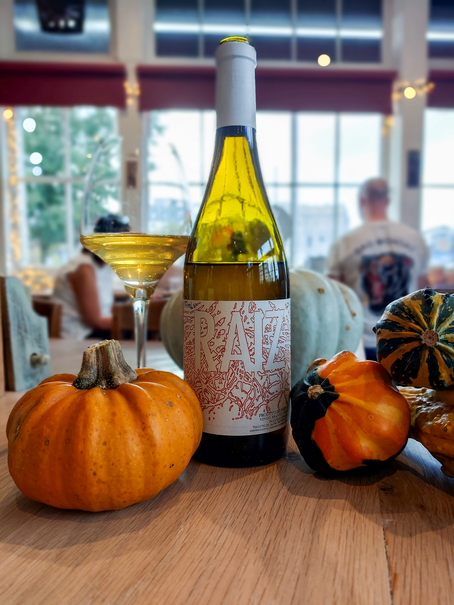 A bottle of Tiago Teles Raiz on a bar counter with autumn squashes